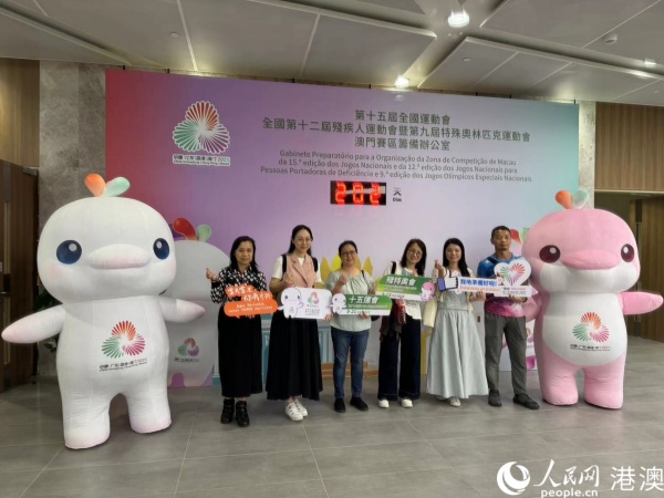 圖為參加培訓(xùn)的澳門賽區(qū)部分志愿者在倒計時牌前，與賽事吉祥物合影。人民網(wǎng)記者 富子梅攝