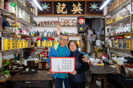 12月18日，澳門(mén)英記茶莊的傳承人盧石麟（左）與夫人在展示祝福語(yǔ)。