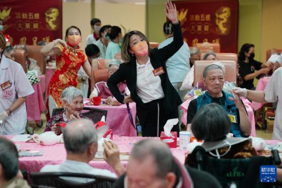 5月24日，在香港松悅園耆和護養(yǎng)院，安老事務(wù)委員會委員、香港樂齡社企“軟餐俠”創(chuàng)辦人文慧妍（中，穿黑色外套）帶領(lǐng)職員扮演成“茶樓”經(jīng)理、廚師和接待員，為老人家提供沉浸式茶樓就餐體驗。新華社發(fā)（王申 攝）