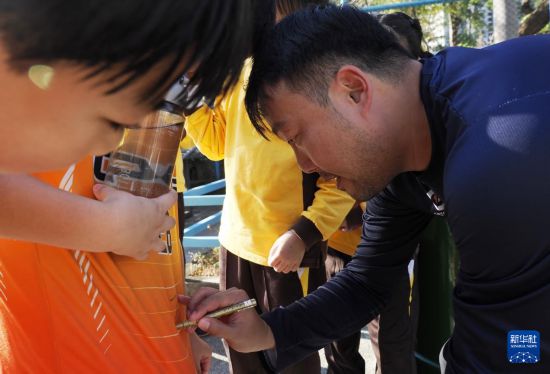 在香港新蒲崗彩虹道150號的露天游樂場，香港男子手球隊主教練許文邦（右）在給小學(xué)生簽名（2025年12月17日攝）。新華社發(fā)（王申攝）